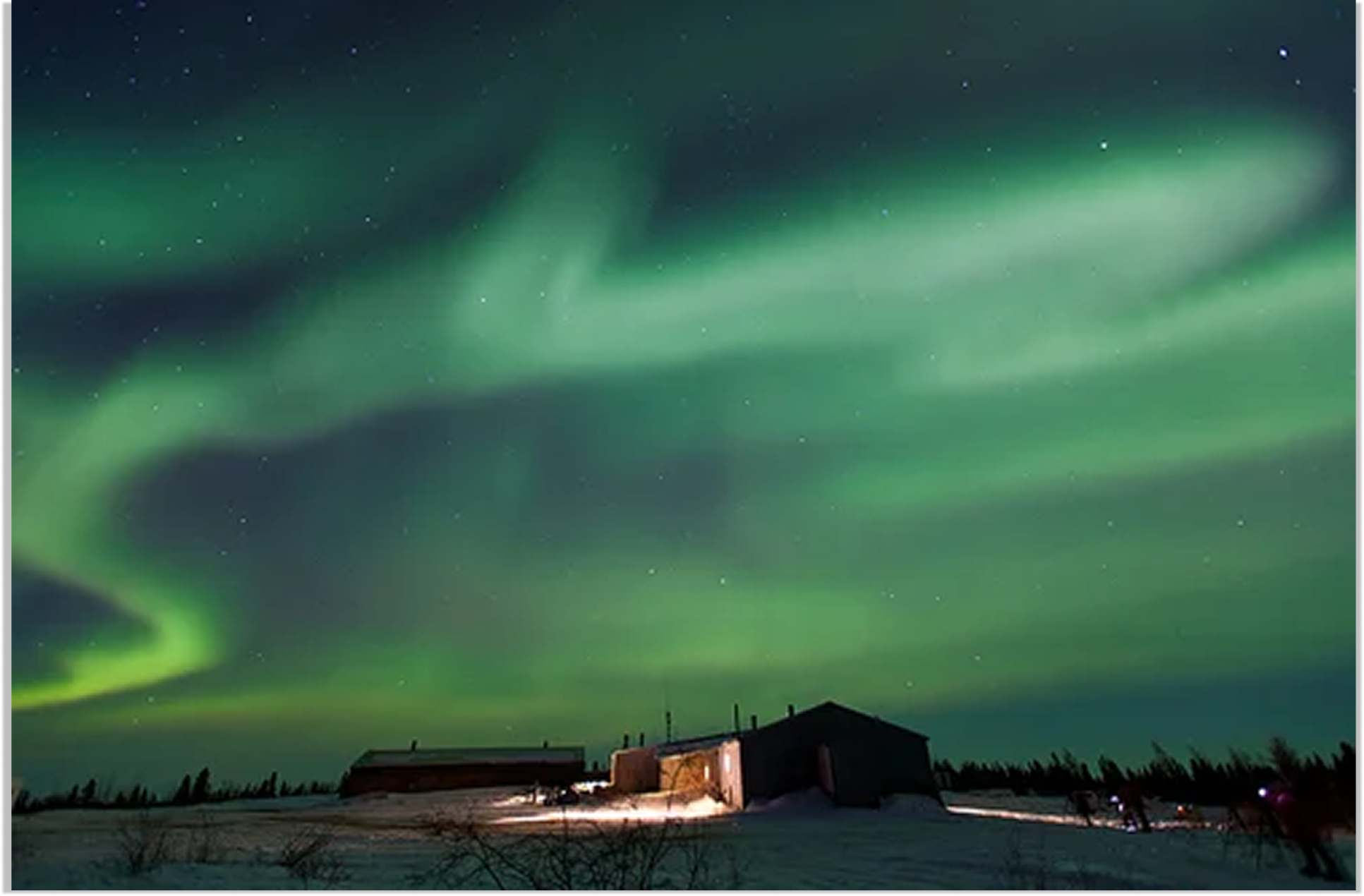 The northern lights in vibrant greens above the lodge which is lit with a soft light